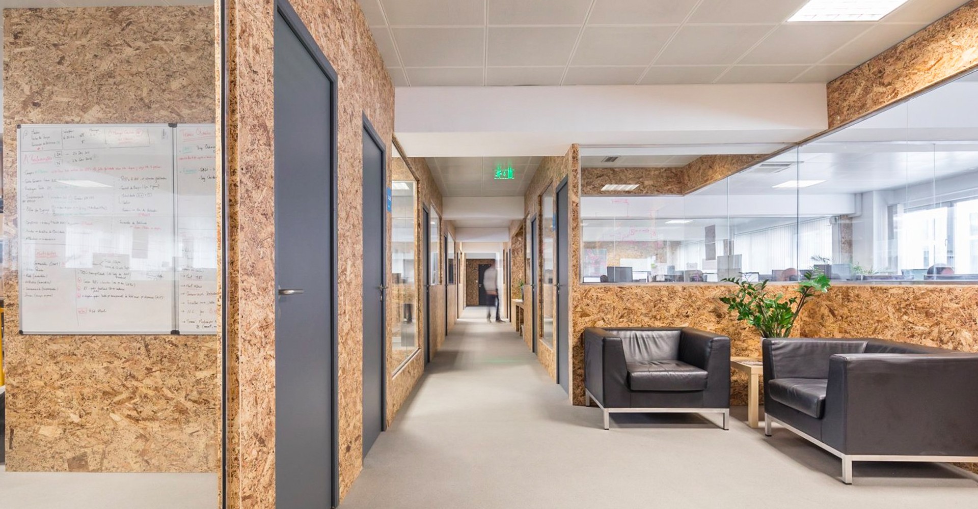 An empty and long hall at Premium Minds' office. There's a small lounge, with couches and a small table with a plant on it, and multiple doors and windows to the various development teams' working areas.