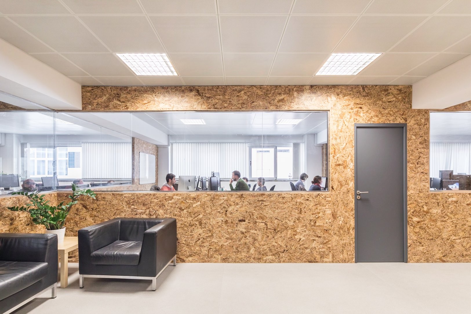 An empty and long hall at Premium Minds' office. There's a small lounge, with couches and a small table with a plant on it, and multiple doors and windows to the various development teams' working areas.